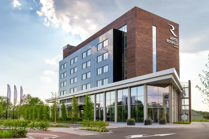 Modern facade of Hotel Rosveld with glass sections and a brick front under a lightly clouded sky